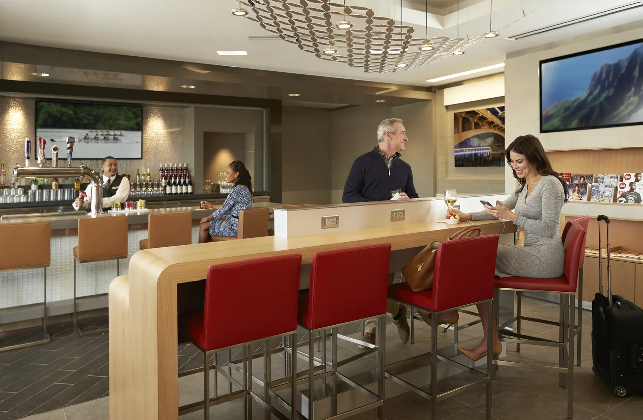 Travellers seated at an Admirals Club bar, the kind of peak-hour occupancy that triggers capacity holds at the door.