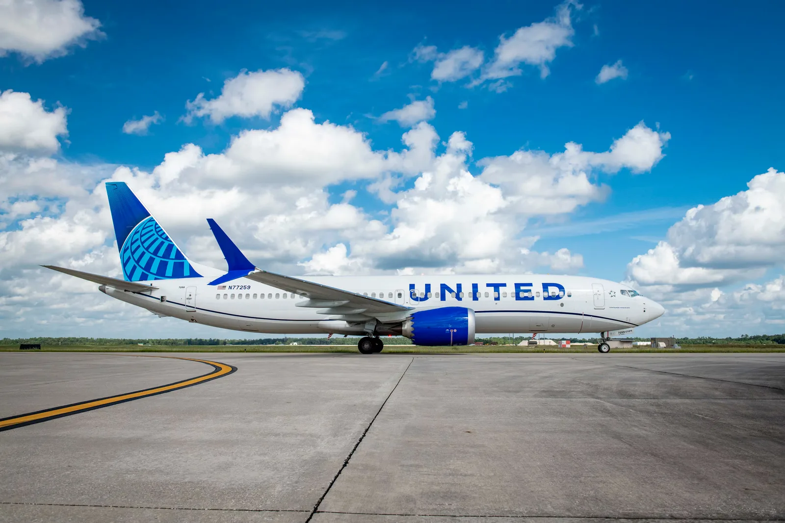 United Airlines Boeing 737 MAX 8 in the current white and blue livery on an airport apron under a blue sky with white clouds