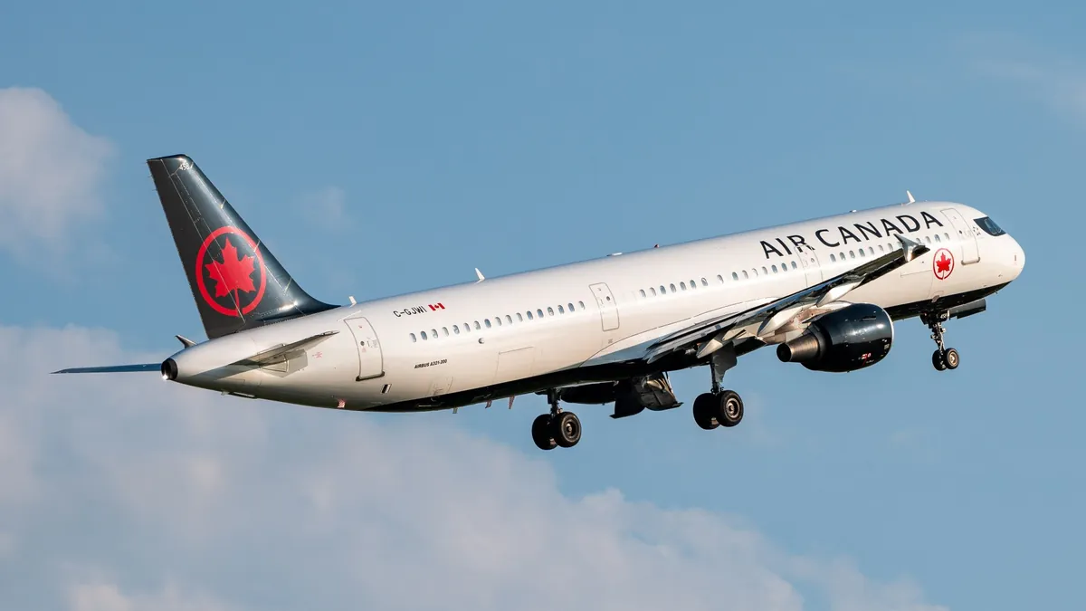 An Air Canada Airbus A321 climbing after take-off against a blue sky with white cloud, its landing gear still extended