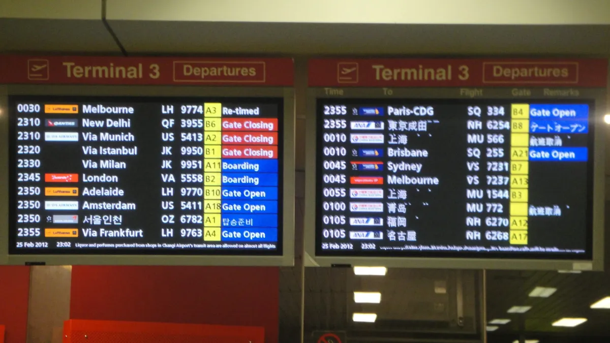 Two airport departure boards showing live flight times, gates and status against a dark terminal wall