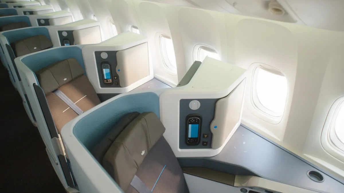 An empty KLM World Business Class cabin on a Boeing 777, rows of shell suites beside large windows in bright daylight