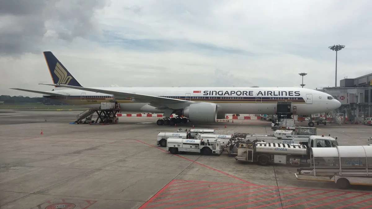 Singapore Airlines Boeing 777-300ER parked at a gate at Singapore Changi Airport, with ground-handling vehicles in the foreground