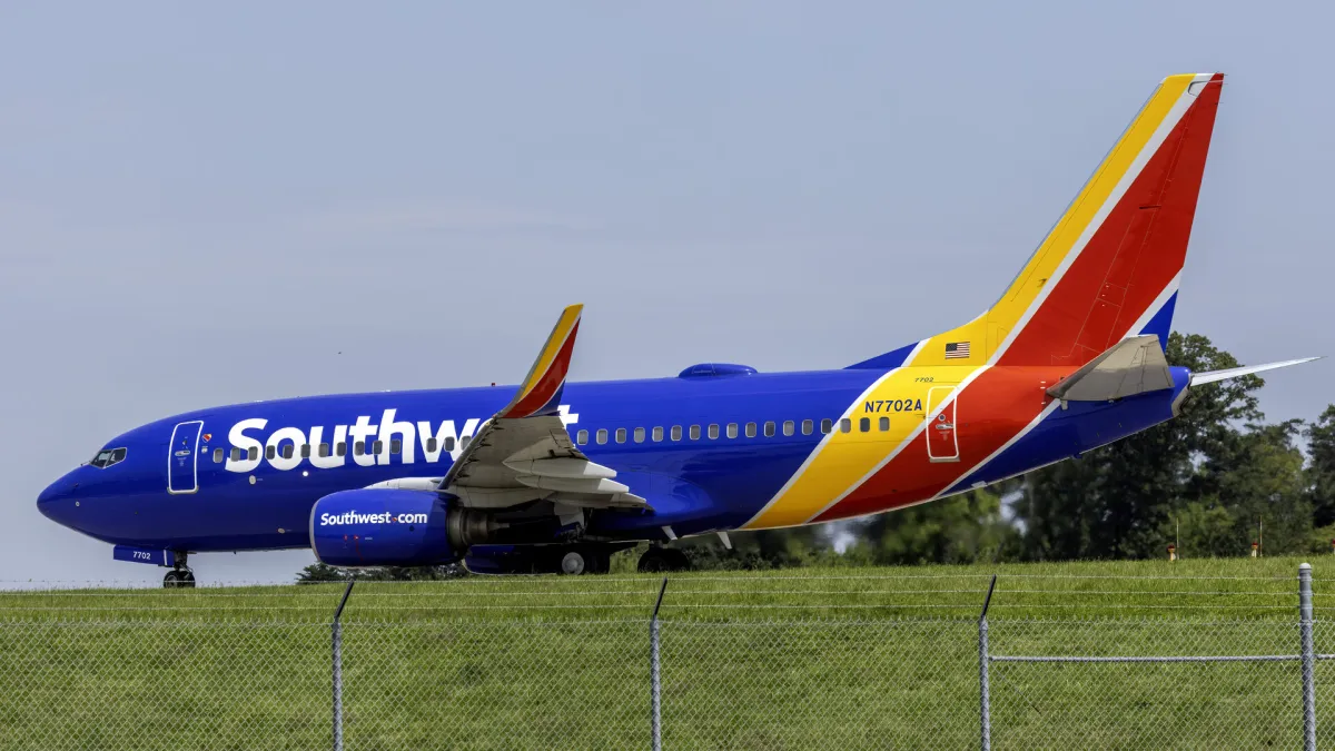 Southwest Airlines Boeing 737-700 in blue, red and yellow Heart livery taxiing past a grass verge and perimeter fence