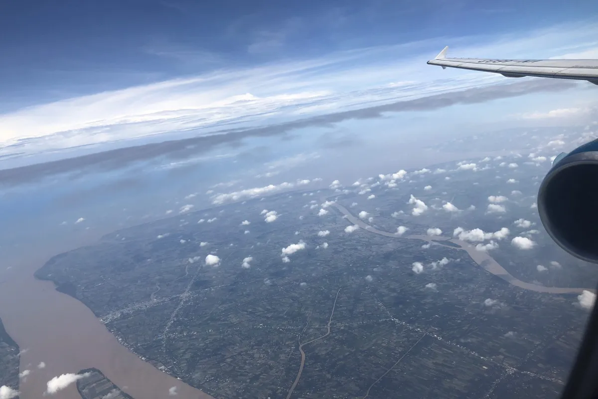 Aerial view of farmland and a river from an aircraft window at cruising altitude.