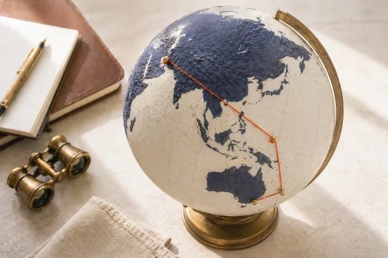 Vintage world globe with brass pins and an orange thread tracing an ultra-long-haul flight route