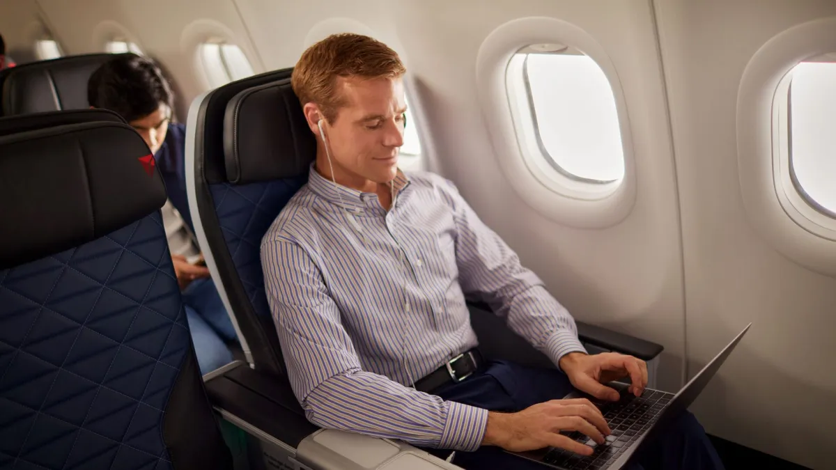 A traveller working on a laptop in a premium economy seat beside the cabin window, checking details before committing