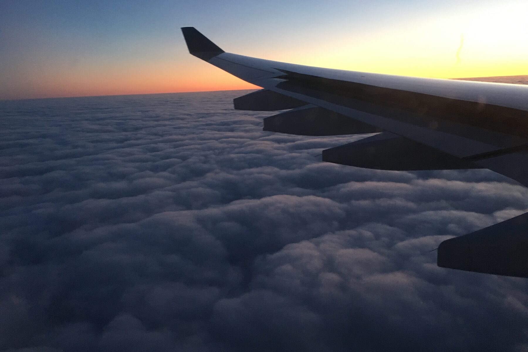 An aircraft wing above a blanket of cloud at sunset.